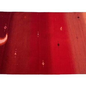 Könnte beinhalten: Ein rechteckiger Teppich mit einem Farbverlauf von dunklem Burgunder bis Orange. Der Teppich hat ein Halbmond-Design und kleine, rautenförmige Muster. Quasten sind an den Ecken sichtbar.