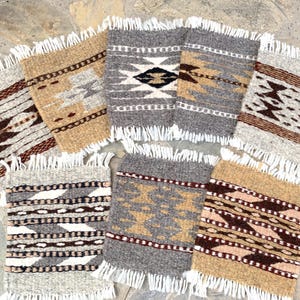 May include: A collection of woven coasters with geometric patterns. The coasters feature various color schemes, including brown, gray, and beige, with white fringe edges. The designs include diamond and zigzag patterns, adding a rustic touch to the home decor.