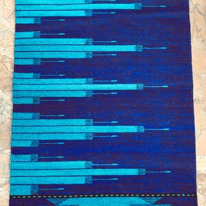May include: A blue and turquoise woven rug with a geometric pattern. The rug has a fringe border.