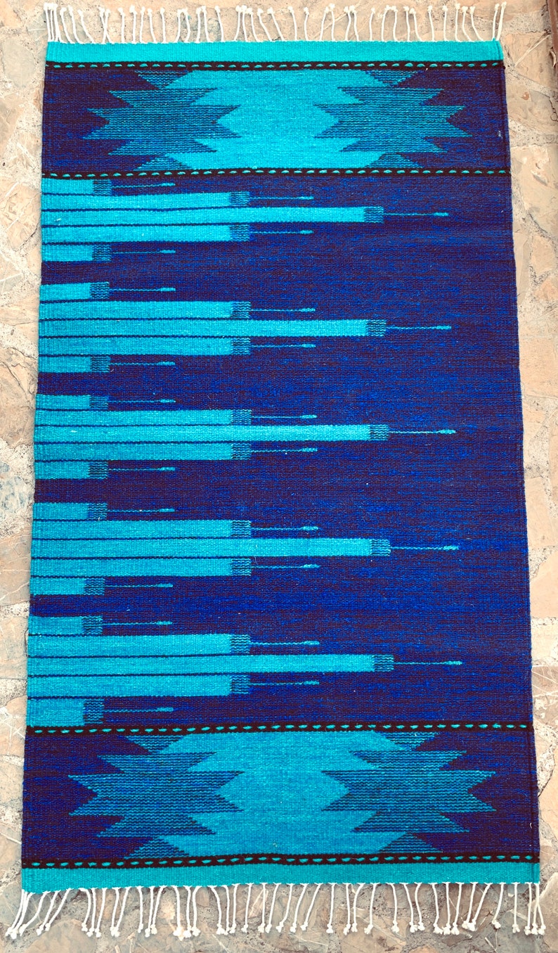 May include: A blue and turquoise woven rug with a geometric pattern. The rug has a fringe border.