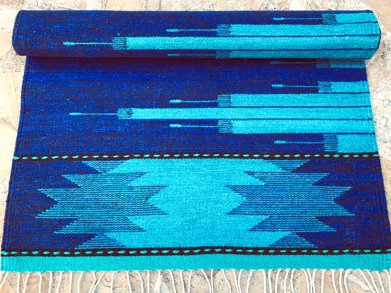 May include: A blue and turquoise woven rug with a geometric pattern. The rug has a fringe on the bottom edge.