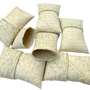 May include: A group of eight woven straw pouches, some are folded closed and some are open, showing the inside. The pouches are all made of a light beige straw.