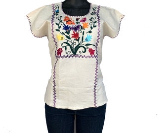 May include: A white cotton blouse with short sleeves and a floral embroidery design. The embroidery features colorful flowers, butterflies, and green leaves.
