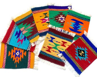 May include: A collection of colorful, woven coasters with geometric patterns and fringed edges. The coasters feature vibrant hues of red, blue, green, yellow, and orange, creating a Southwestern or tribal aesthetic. Each coaster is approximately 4 inches square.