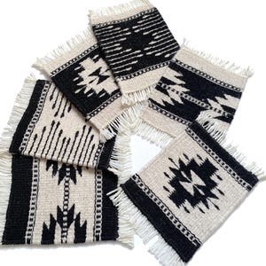 May include: A collection of six square woven coasters with a black and cream geometric pattern. Each coaster has a fringed edge. The coasters are arranged on a white background.