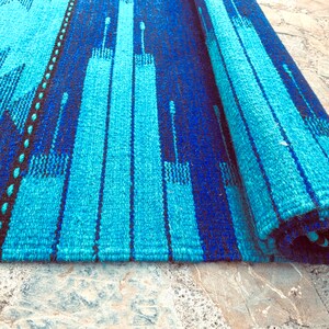 May include: A blue and black striped rug with a geometric pattern. The rug is rolled up and the edges are visible.