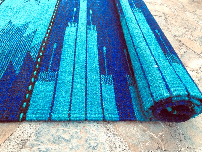 May include: A blue and black striped rug with a geometric pattern. The rug is rolled up and the edges are visible.