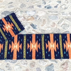 Peut inclure: Un tapis long et étroit avec un motif géométrique dans des tons d'orange, noir, jaune et bleu. Le tapis a des franges aux deux extrémités.