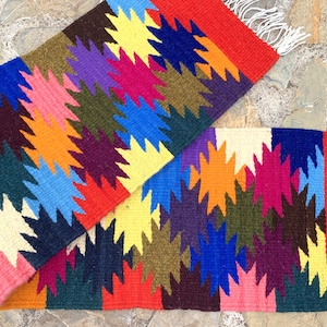 Peut inclure: Un tapis tissé coloré avec un motif géométrique d'étoiles dans des tons de rouge, orange, jaune, vert, bleu, violet et blanc.