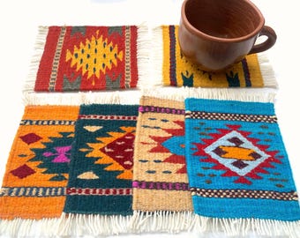 May include: A set of six rectangular woven coasters featuring various geometric patterns in vibrant colors including red, yellow, orange, teal, and tan, each finished with white fringe on the short ends, with a brown ceramic mug on one coaster.