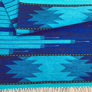 May include: A blue and black woven rug with a geometric pattern. The rug has a fringe on the bottom edge.