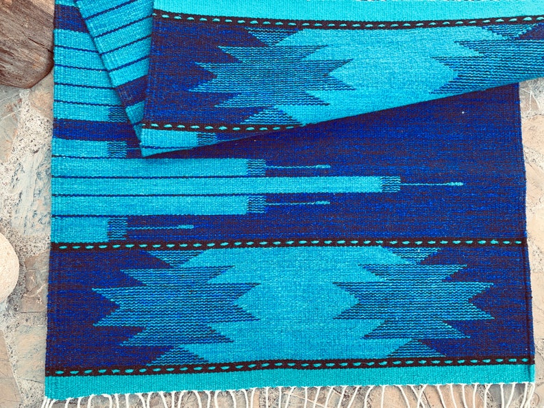 May include: A blue and black woven rug with a geometric pattern. The rug has a fringe on the bottom edge.
