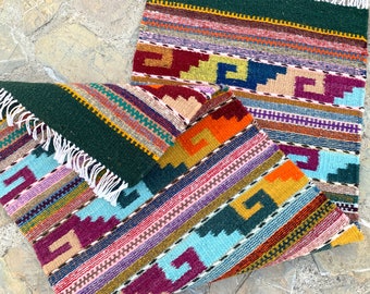 May include: Two colourful woven rugs with geometric patterns in shades of green, blue, orange, red, and purple. The rugs have fringe on the edges.