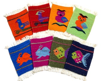 May include: A collection of eight colorful woven coasters, each featuring a different animal design. The coasters have fringed edges and include images of birds, owls, rabbits, and fish. The background colors vary, including orange, red, blue, green, and pink.