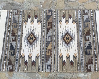 May include: A white, brown, and gray woven rug with a geometric pattern. The rug has fringe on all four sides.