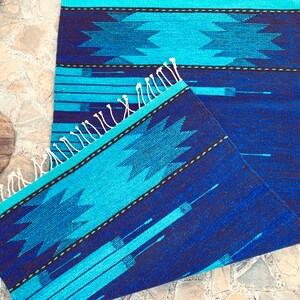 May include: A blue and turquoise woven rug with a geometric pattern. The rug has a fringe border and is folded in half.