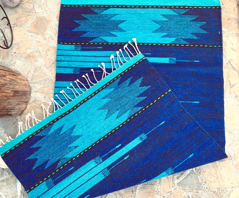 May include: A blue and turquoise woven rug with a geometric pattern. The rug has a fringe border and is folded in half.