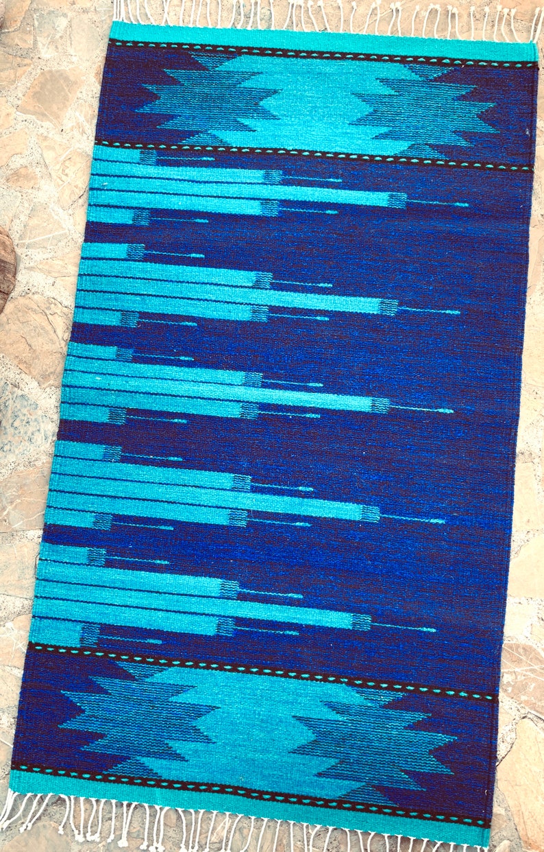May include: A blue and turquoise woven rug with a geometric pattern. The rug has a fringe border.