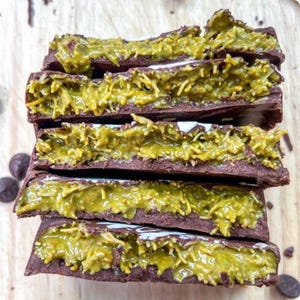 Könnte beinhalten: Fünf Schokoladenriegel, die übereinander gestapelt sind, jeder Riegel ist mit einer grünen, faserigen Füllung gefüllt, die an Kokosnuss erinnert.