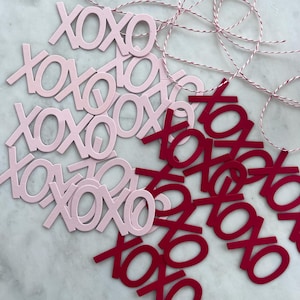 May include: Pink and red XOXO cutouts with red and white twine. The pink cutouts are grouped, while the red ones are scattered. The twine is twisted and looped, suggesting a decorative or craft project.