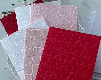 May include: A set of six embossed cards with different heart patterns. The cards are in shades of pink, white, and red. The cards are arranged in a stack, with the red card on top. The cards are surrounded by small, colorful sequins. The text "THE CARD CHEMIST" and "HANDMADE BY MICHELLE" is visible at the bottom of the image.