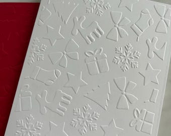 May include: A white card with embossed Christmas-themed designs, including snowflakes, bows, stars, gift boxes, stockings, and reindeer. A red card is visible in the background, with a silver bell and ornament in the upper right corner.