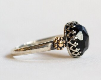 May include: A silver ring with a black gemstone set in a gold and silver crown design.