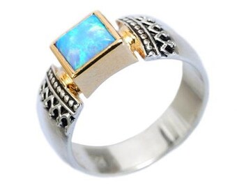 May include: A silver ring with a square blue opal gemstone set in a gold band. The ring has a decorative design on the band.