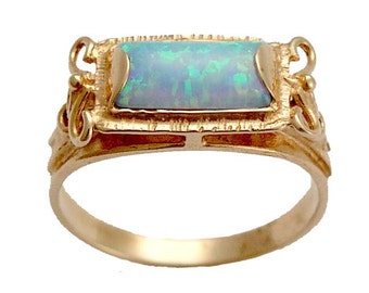 May include: A gold ring with a rectangular opal gemstone set in a detailed frame. The ring has a delicate design with intricate details.
