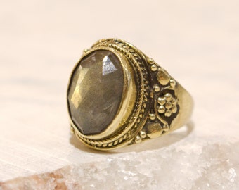 May include: A gold ring with a large, faceted, gray gemstone set in a decorative, ornate setting.