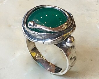 May include: A silver ring with a green gemstone set in a textured, twisted band.