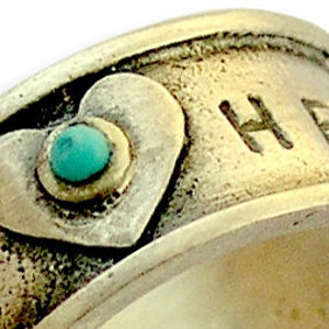 May include: Silver ring with a turquoise stone set in a heart shape. The ring is engraved with the word "HOPE".