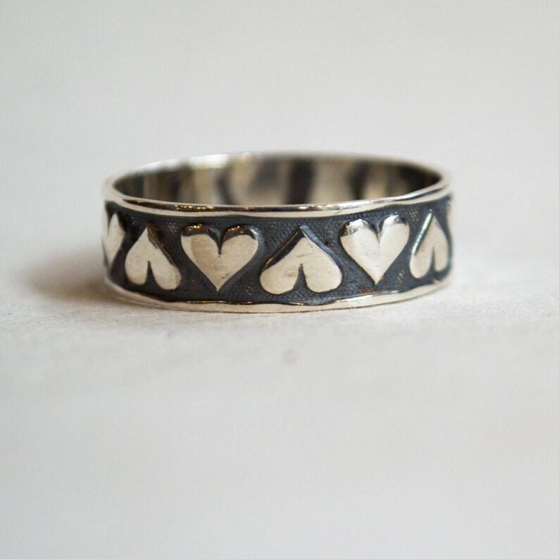 May include: A silver ring with a black band and a row of heart-shaped cutouts.