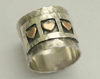 May include: A silver ring with a textured band and three gold heart accents. The hearts are set in rectangular frames.