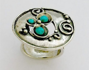 May include: A silver ring with a circular design featuring three turquoise stones set in a floral pattern.