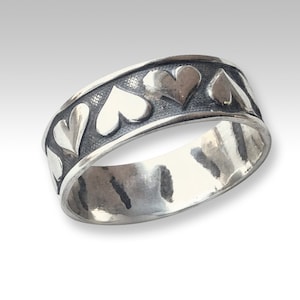 May include: A silver band ring with a textured finish and a row of raised heart designs around the band.