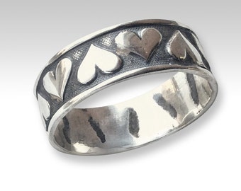 May include: A silver band ring with a textured finish and a row of raised heart designs around the band.