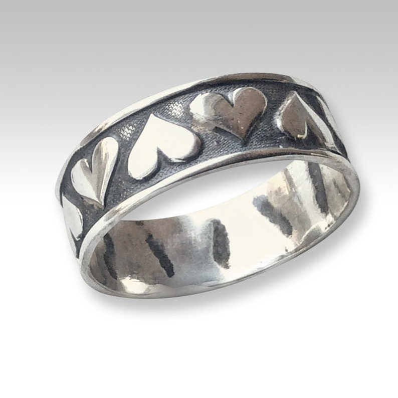 May include: A silver band ring with a textured finish and a row of raised heart designs around the band.