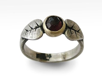 May include: A silver ring with two leaf-shaped accents on either side of a red gemstone set in a gold bezel.