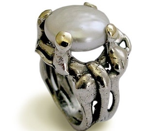 May include: A silver ring with a large white pearl set in the center. The ring is designed with two silver bands that wrap around the pearl, and the bands are accented with gold.