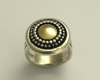 May include: A silver ring with a gold center and a textured design. The ring is round and has a raised edge.