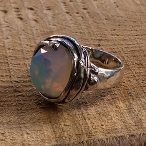 Puede incluir: Un anillo de plata con una gran piedra de ópalo iridiscente engastada en una banda de plata retorcida.