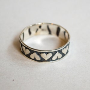 May include: A silver ring with a black band and a row of silver hearts around the band.