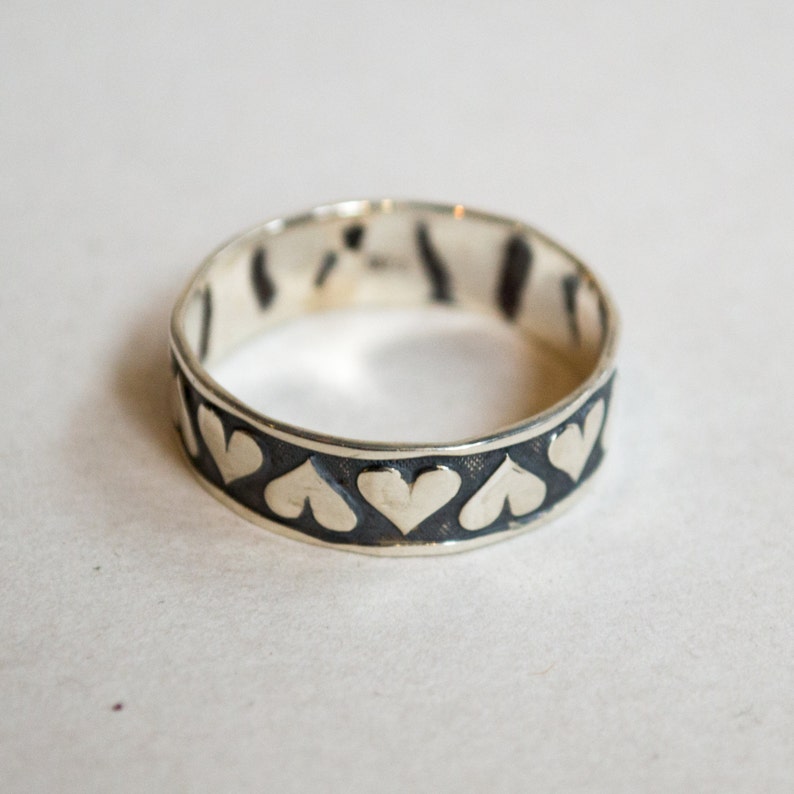 May include: A silver ring with a black band and a row of silver hearts around the band.