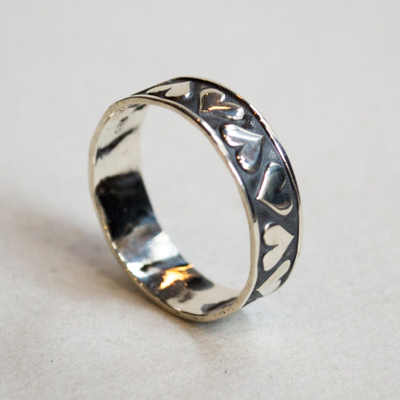 May include: A silver ring with a band decorated with a repeating pattern of hearts.