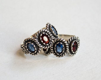 May include: A silver ring with a twisted design and blue and red gemstones.