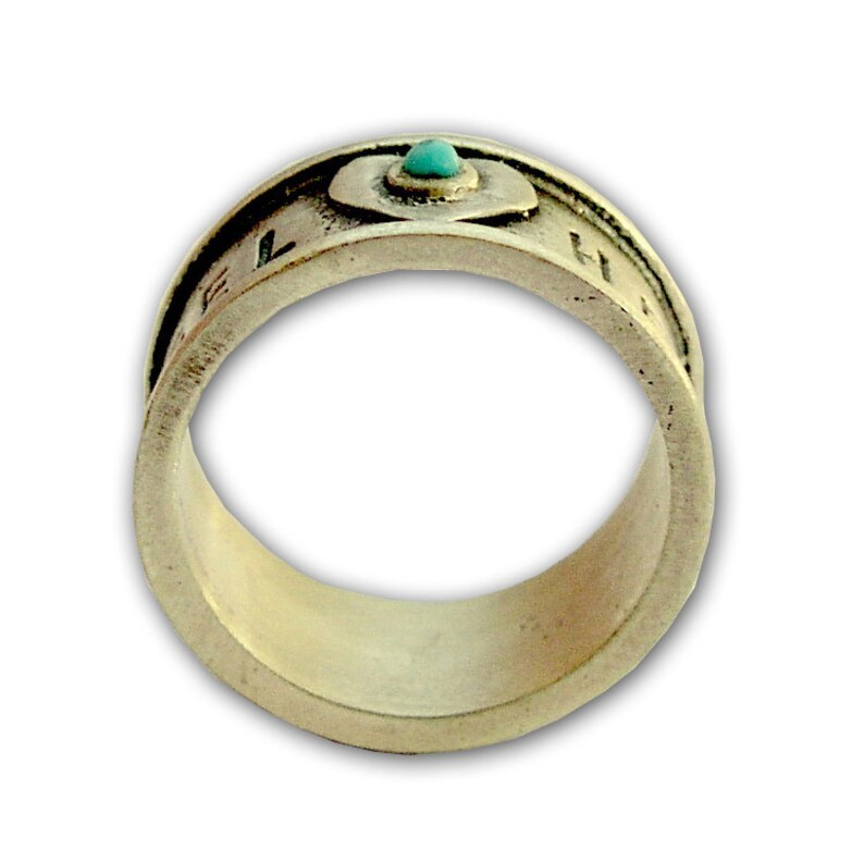 May include: A silver ring with a turquoise stone set in a heart-shaped design. The ring is inscribed with letters around the band.