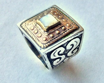 May include: A silver ring with a square-shaped, white stone set in a gold frame. The ring has intricate designs around the stone and on the band.
