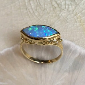 Könnte beinhalten: Ein goldener Ring mit einem Marquise-förmigen Opal-Edelstein. Der Opal ist hellblau mit grünen und blauen Schimmern.