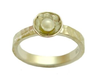 May include: A silver ring with a hammered texture and a round, slightly raised setting that holds a white pearl.